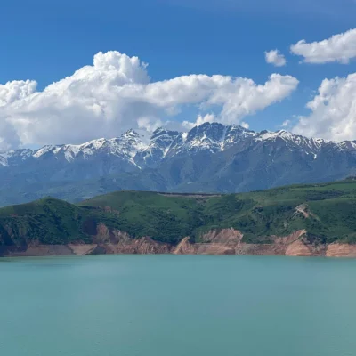 Montagne innevate si ergono sopra un lago turchese sotto un cielo azzurro con nuvole bianche, un panorama suggestivo.