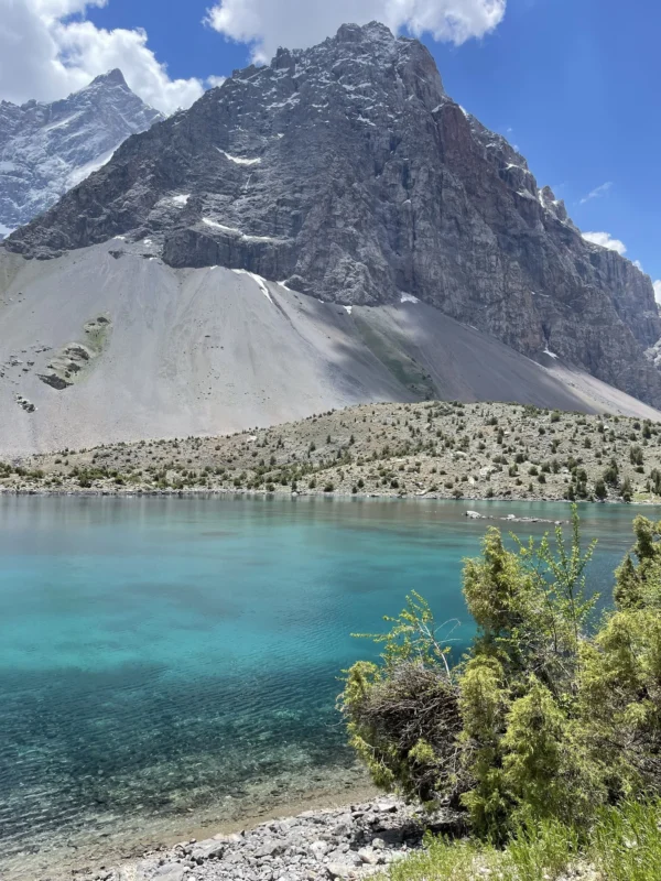 Lago alpino turchese con sponde rocciose e montagne frastagliate sotto un cielo azzurro con nuvole.